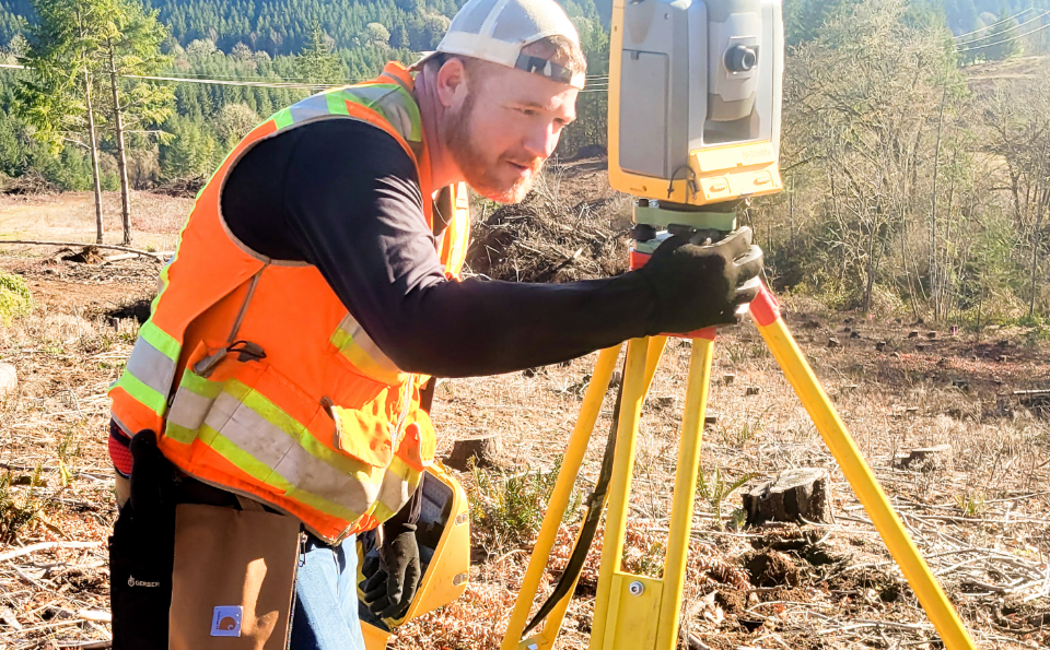 AKS Engineering team member in orange vest at project site using surveying equipment