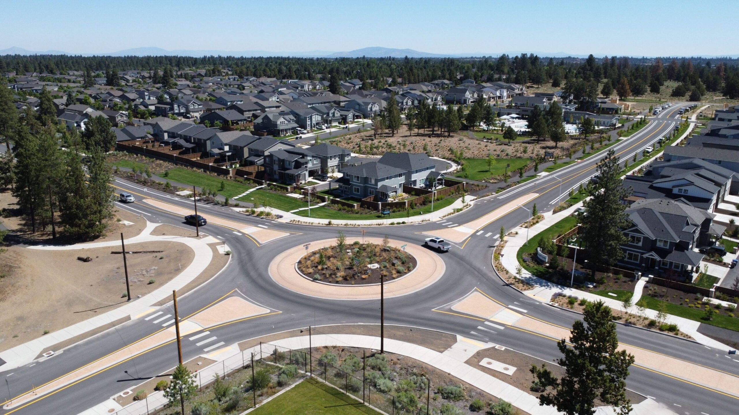 Aerial view of the Caldera Roundabout along SE 15th Street in Southeast Bend, Oregon, showing the single-lane roundabout connecting nearby neighborhoods, open fields, and natural areas with walking trails near Caldera High School.